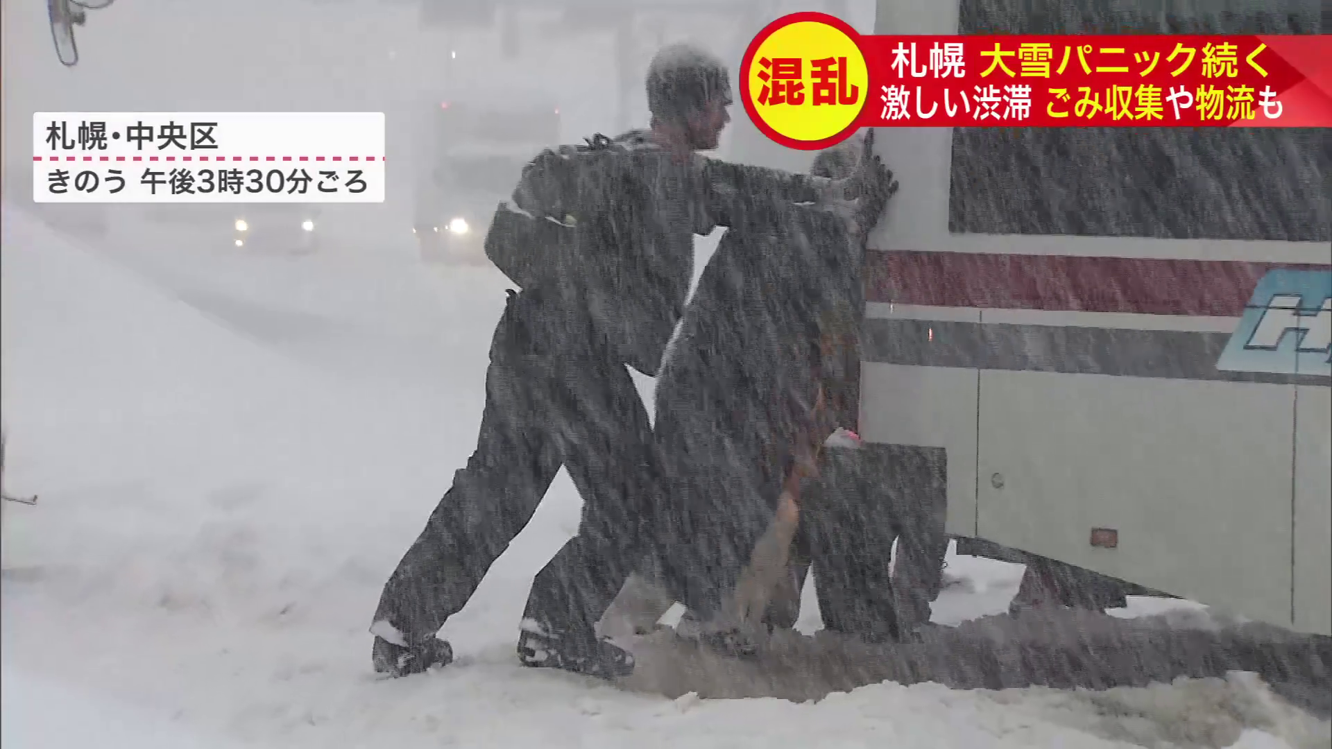 雪にはまったバスを押す観光客たち